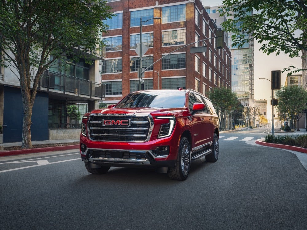 The 2026 GMC Yukon XL Elevation is featured in Volcanic Red Tintcoat, in an urban setting during daytime.