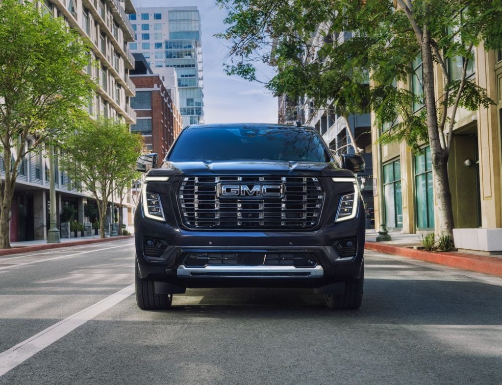 2026 Yukon Denali Ultimate Rush Metallic driving thru city with view of front GMC grille