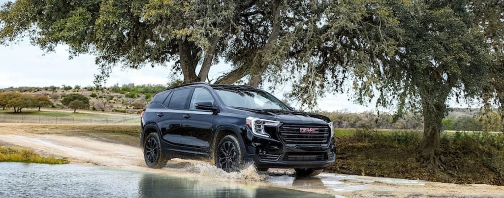 A black 2022 GMC Terrain Elevation is driving through a puddle on a sandy road after visiting used car dealers near Port Lavaca.
