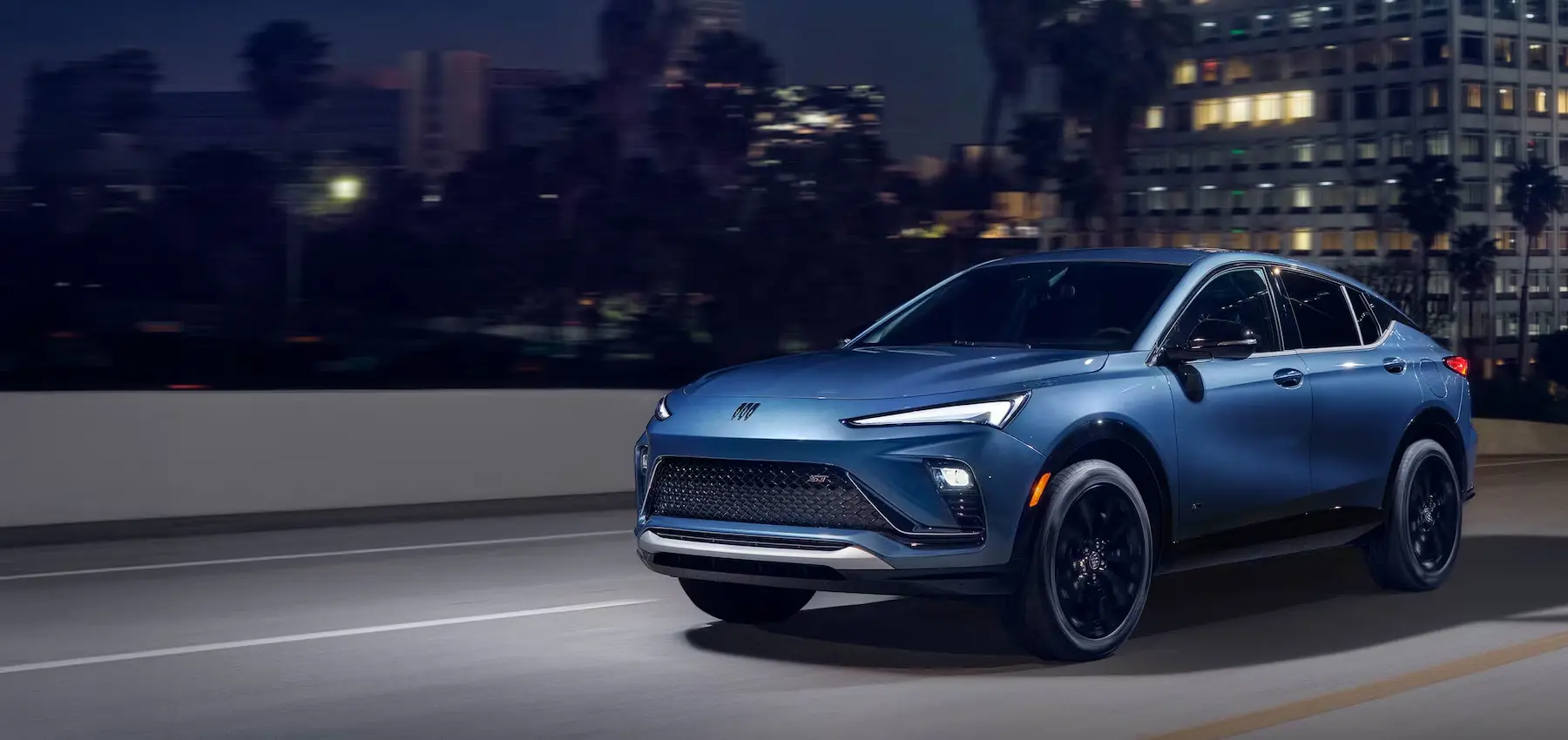 A blue SUV drives along a city road at night, illuminated by urban lights.