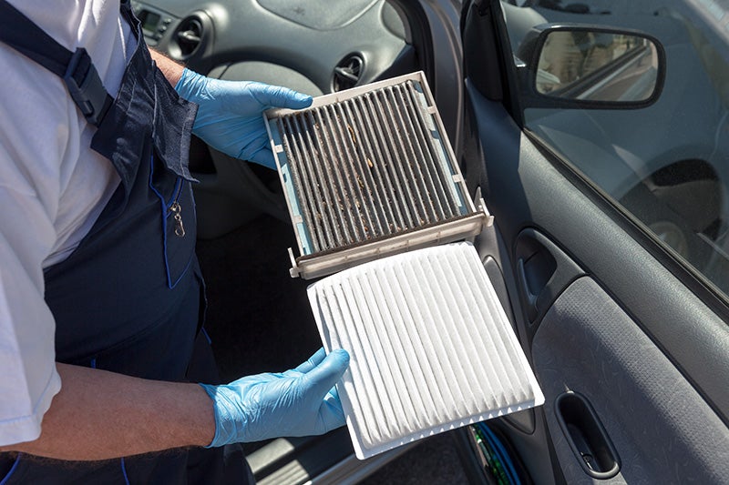 A mechanic holding a dirty car air filter next to a clean white replacement.
