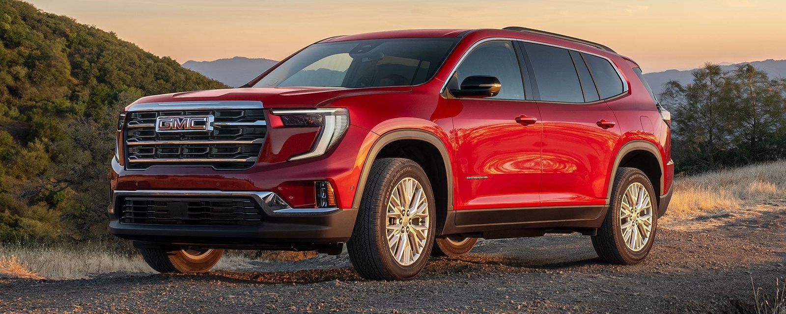 Red 2027 GMC Acadia Elevation parked on a mountain road at sunset; new GMC Acadia SUVs for sale at Ross Downing GMC in Hammond, LA