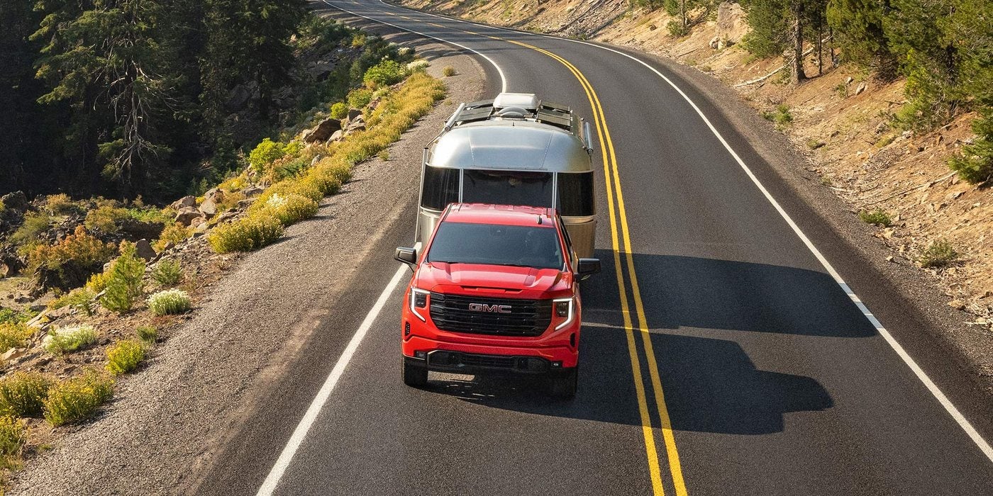 Red 2026 GMC Sierra 1500 towing an Airstream travel trailer on a mountain road; Sierra 1500 towing at Ross Downing GMC in Hammond, LA