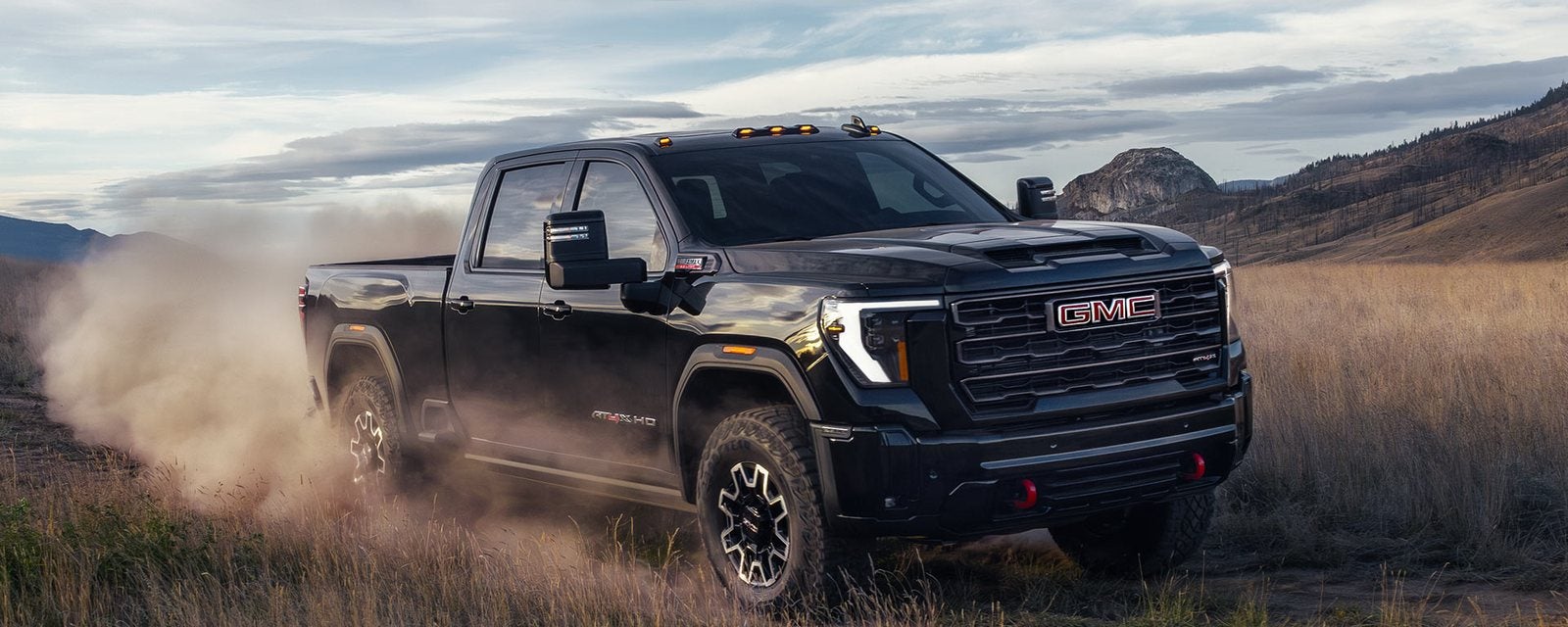 Black 2026 GMC Sierra 2500 HD AT4 kicking up dust on a grassy trail; new GMC Sierra 2500 HD trucks for sale at Ross Downing GMC in Hammond, LA