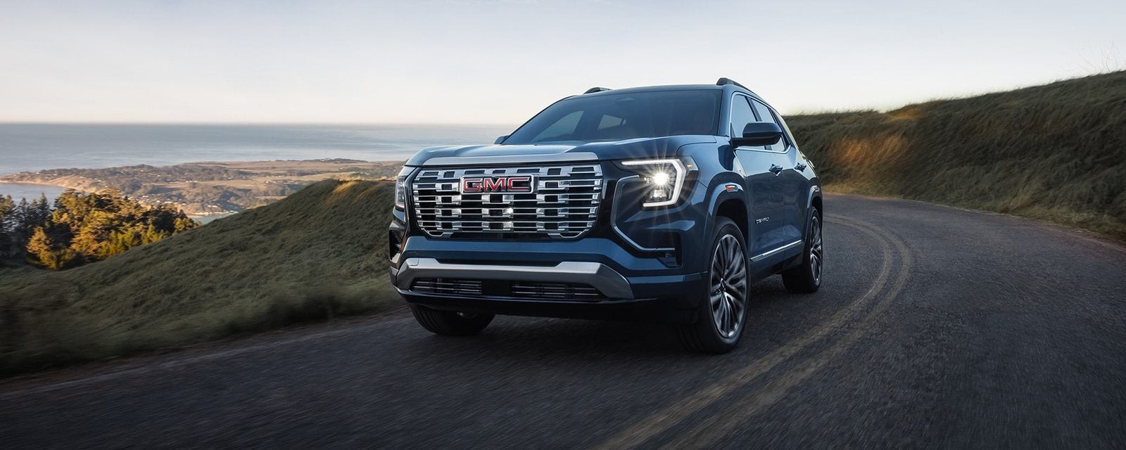 Blue 2027 GMC Terrain Denali on a winding coastal road; new GMC Terrain SUVs for sale at Ross Downing GMC in Hammond, LA
