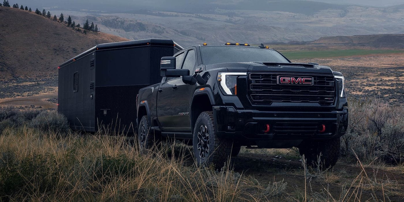 Black 2026 GMC Sierra 2500 HD towing an enclosed trailer across open grassland; Sierra 2500 HD towing at Ross Downing GMC in Gonzales, LA