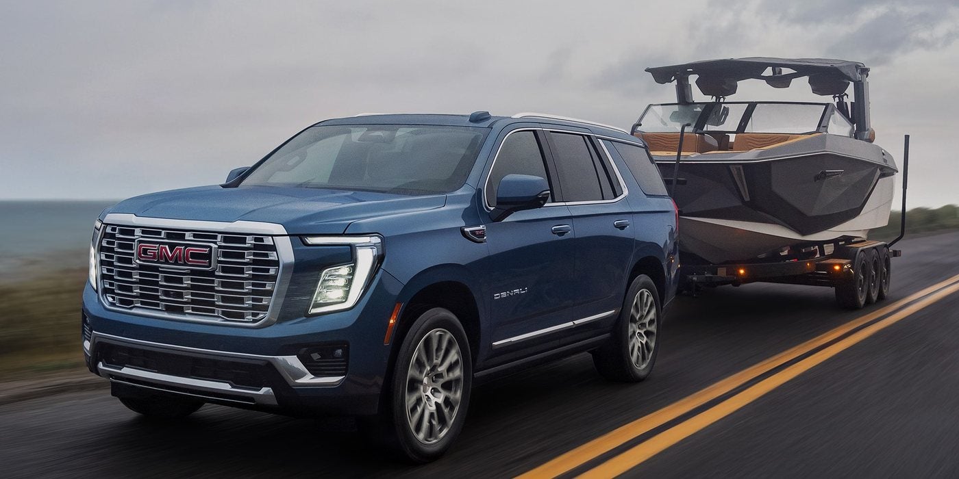 Blue 2027 GMC Yukon towing a boat on a two-lane road; GMC Yukon engines and towing at Ross Downing GMC in Gonzales, LA