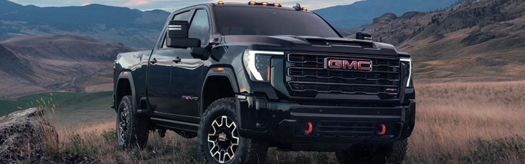 Black GMC pickup truck parked in a grassy hillside landscape with rolling mountains in the background at sunset.