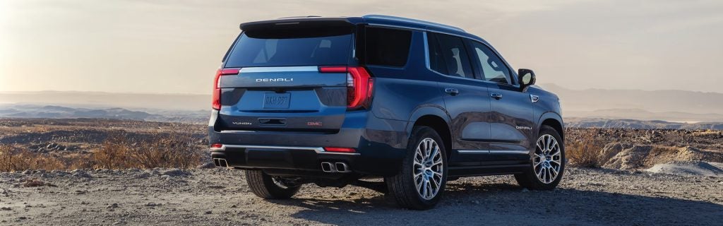 Blue GMC Yukon Denali SUV parked on a rugged landscape with scenic hills in the background.