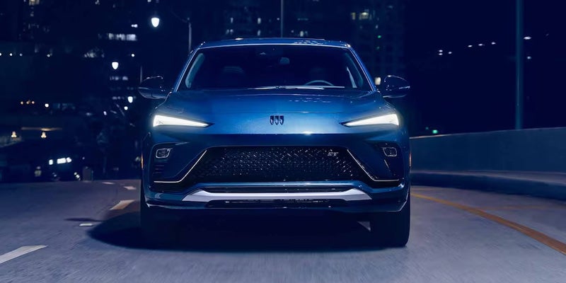 Blue Buick SUV driving on a city road at night with illuminated headlights