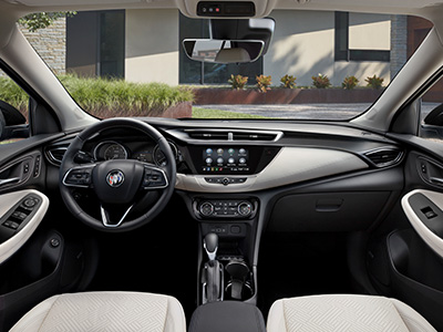 Modern car interior with a sleek dashboard, leather-wrapped steering wheel, touchscreen display, and beige seats. Sunlight filters through large windows.