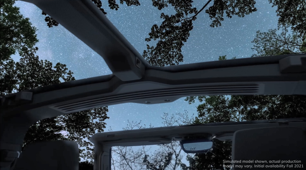 View of a starry night sky and tree branches through a car's open sunroof, conveying a serene, open-air experience in a natural setting.