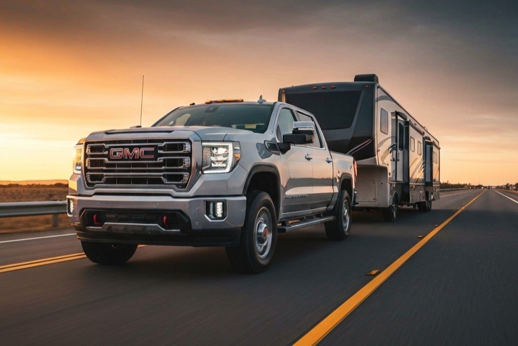 GMC Sierra towing a camper down a road at sunset