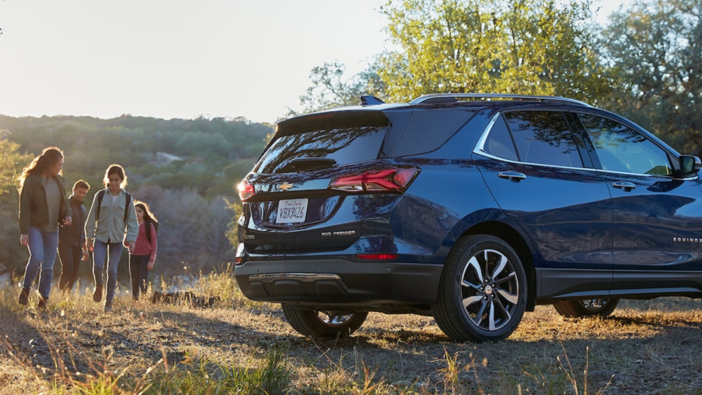 a family of four walks towards a blue suv in a grassy setting