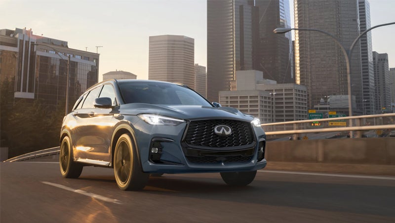 An Infiniti SUV driving on a city highway with tall buildings in the background