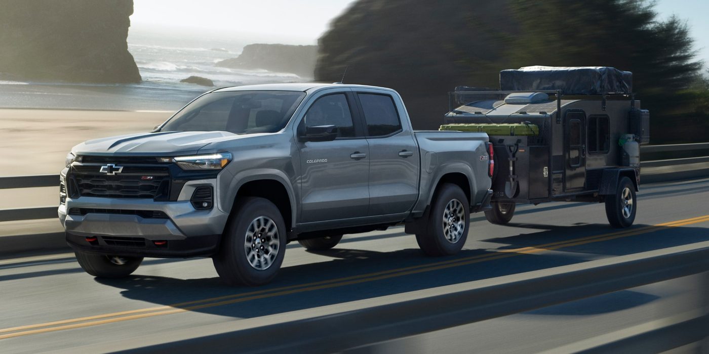 Silver 2027 Chevy Colorado Z71 towing a camping trailer on a coastal highway