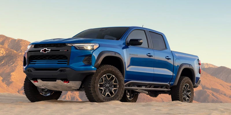 A blue Chevrolet Colorado pickup truck parked in the desert with mountains in the background