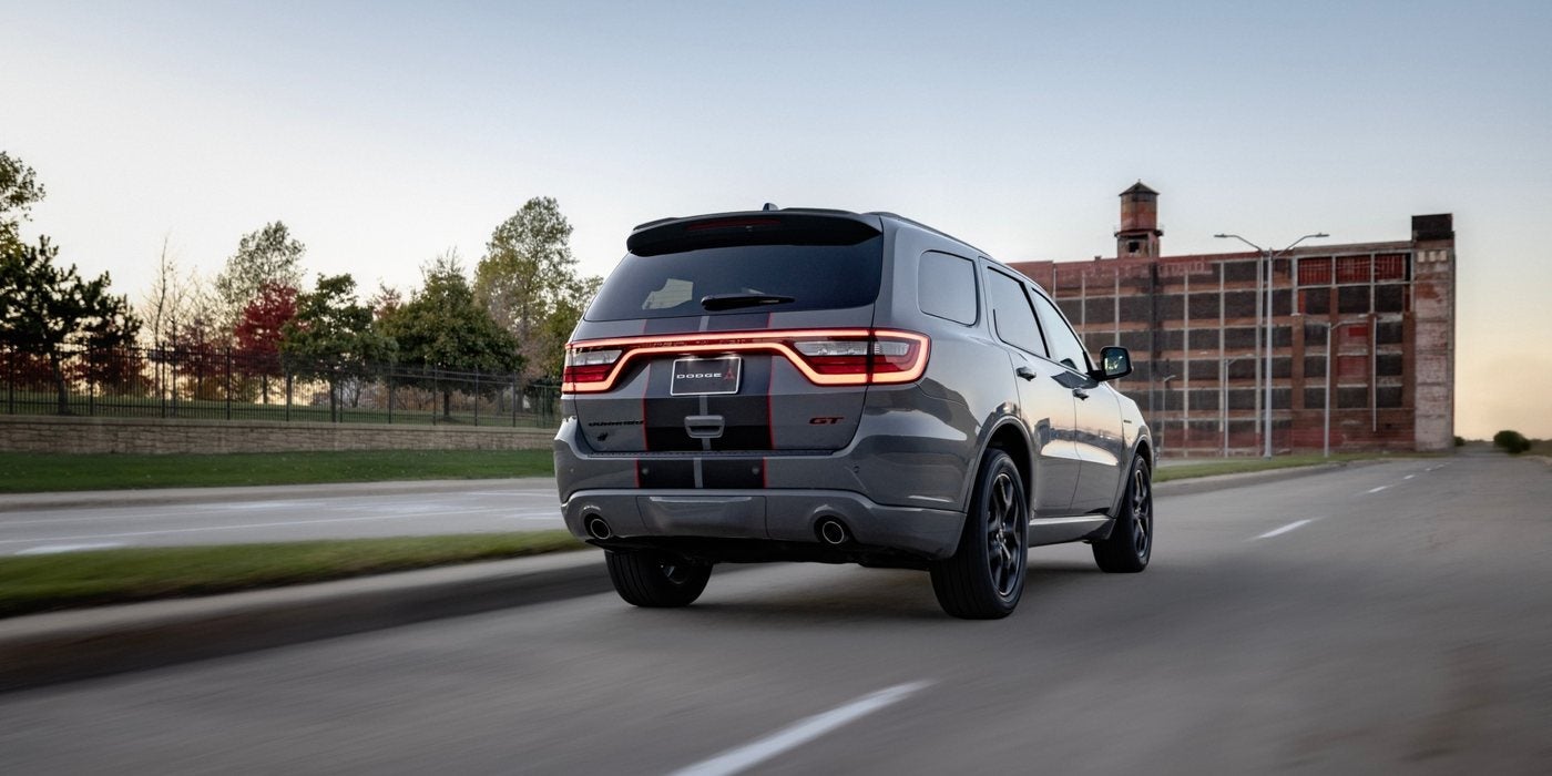 Gray 2027 Dodge Durango GT HEMI V8 with black and red stripes driving past a brick factory; Durango engines and towing at Ross Downing CDJR in Hammond, LA