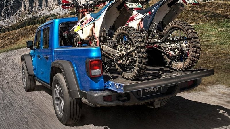 Blue 2026 Jeep Gladiator Sport S hauling two dirt bikes in its bed; Gladiator financing at Ross Downing CDJR in Hammond, LA