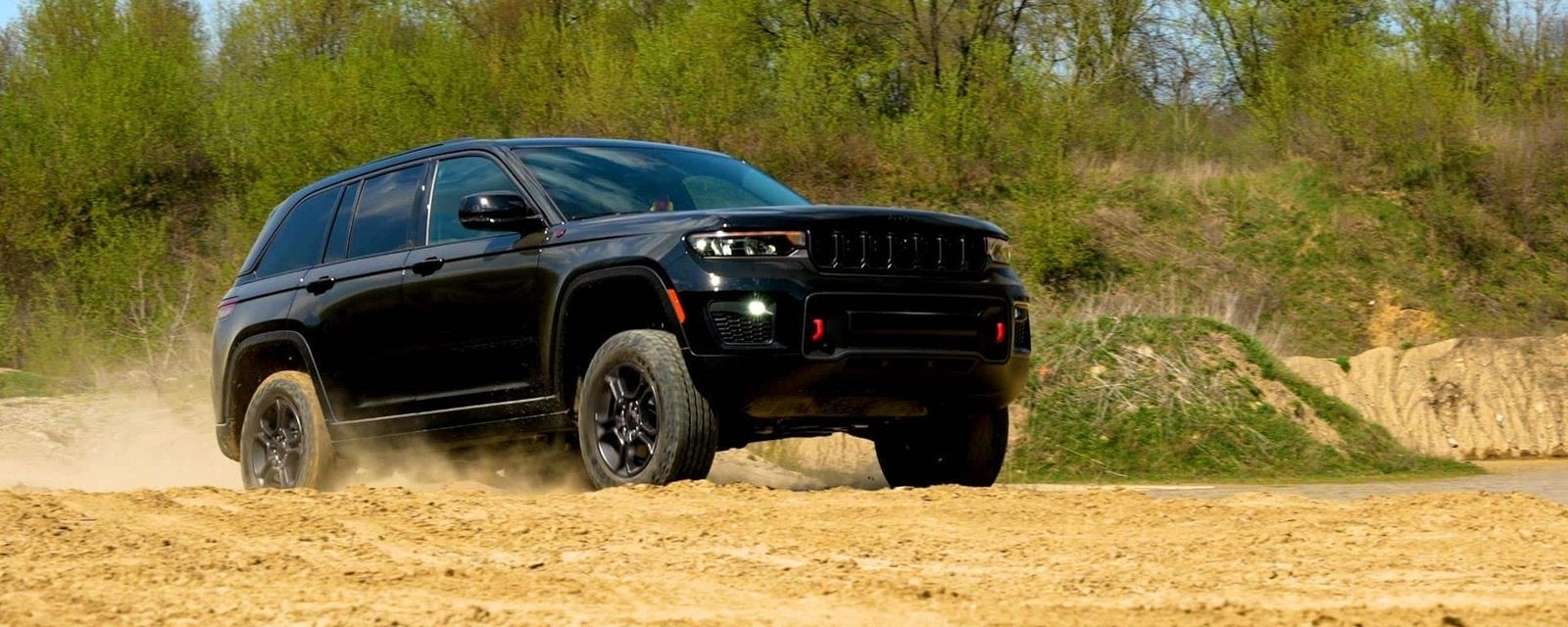 Black 2027 Jeep Grand Cherokee Trailhawk kicking up dust on a sandy trail; new Grand Cherokees for sale at Ross Downing CDJR in Hammond, LA