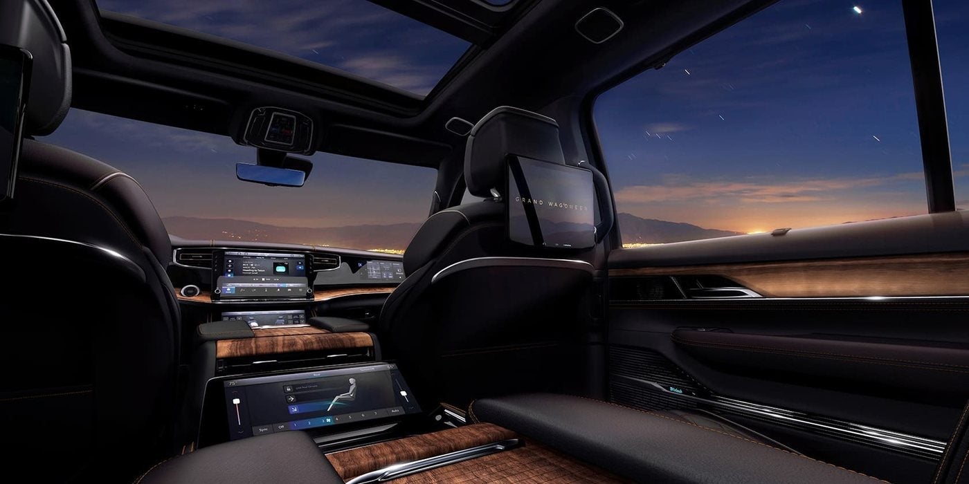 2027 Jeep Grand Wagoneer cabin at dusk with dark leather seats, wood trim, a panoramic sunroof and a seatback entertainment screen, at Ross Downing CDJR in Hammond, LA
