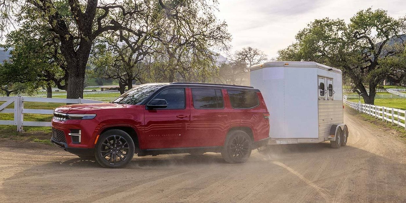 Red 2027 Jeep Grand Wagoneer Summit Obsidian towing a white trailer on a ranch road, for sale at Ross Downing CDJR in Hammond, LA
