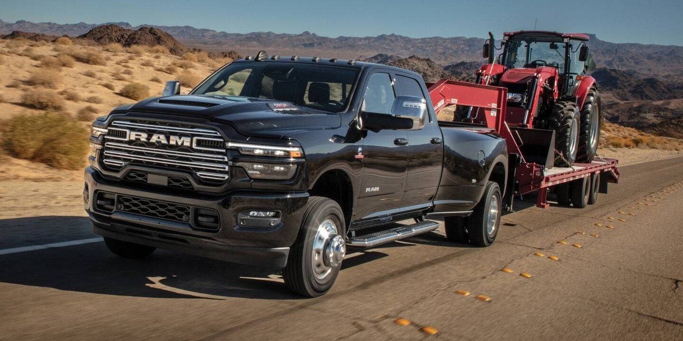 2027 Ram 3500 Laramie dually Crew Cab towing a red tractor on a flatbed trailer through the desert, for sale at Ross Downing CDJR in Hammond, LA