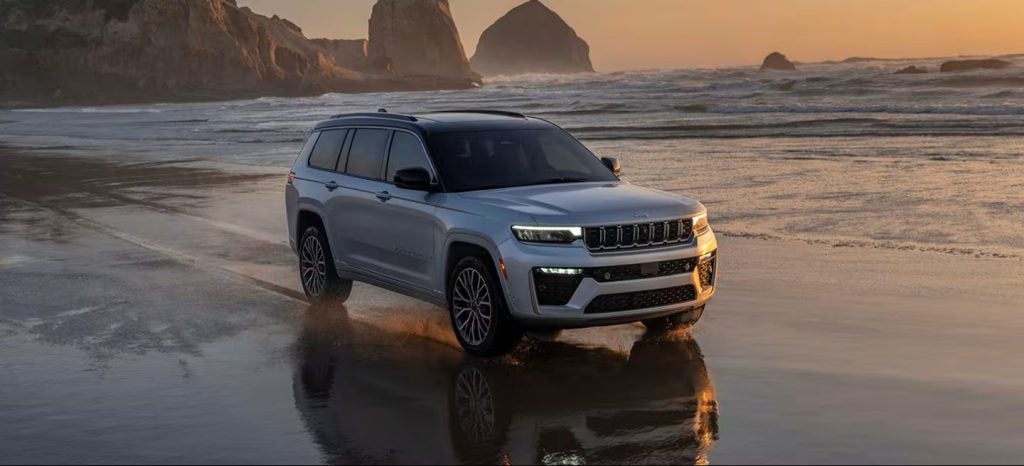 White Jeep SUV driving along a beach shoreline at sunset.