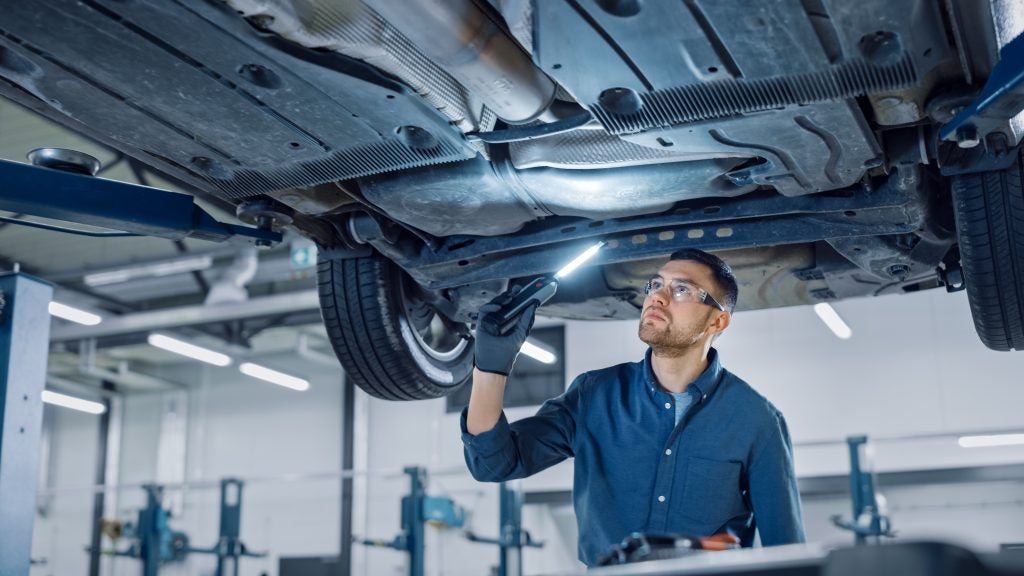 A mechanic inspects the undercarriage of a car using a flashlight in an automotive repair shop.