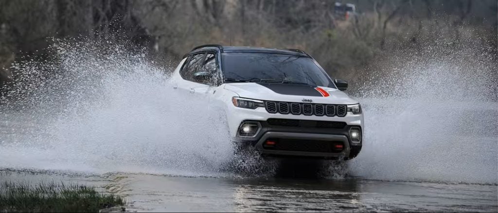 White Jeep SUV driving through water splash outdoors.