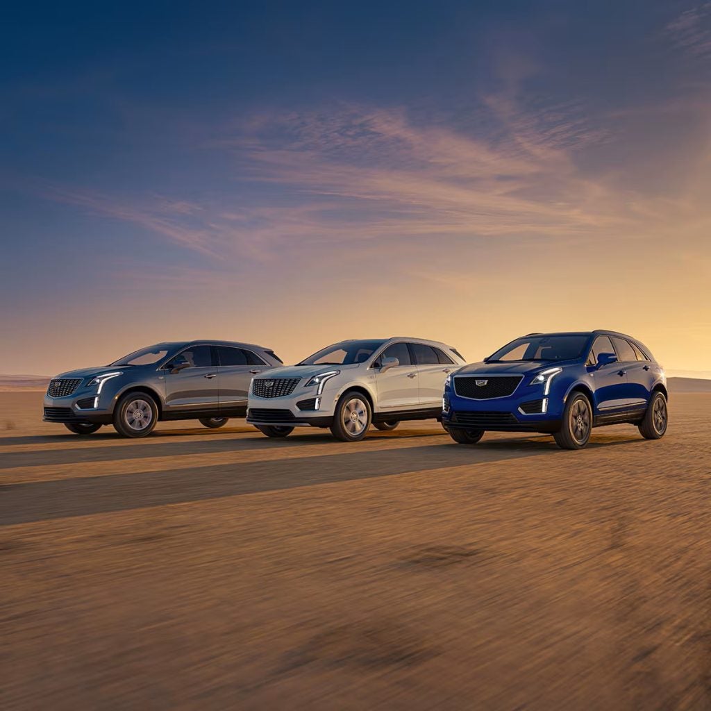 Three Cadillac SUVs driving together on a scenic road at sunset.