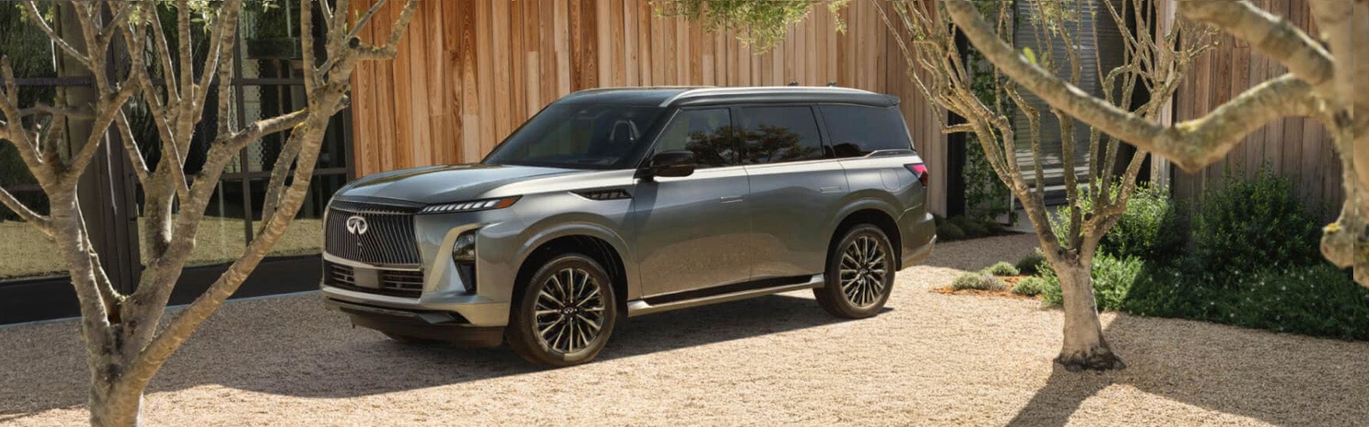 Silver INFINITI QX80 SUV parked on a gravel path.