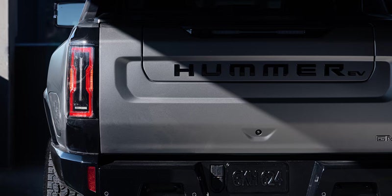 The rear view of a Hummer EV with bold lettering and red taillights, partially in shadow.