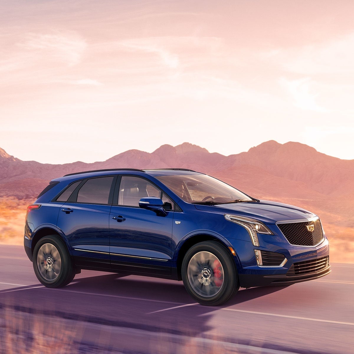 A blue Cadillac SUV driving on a desert road at sunset.