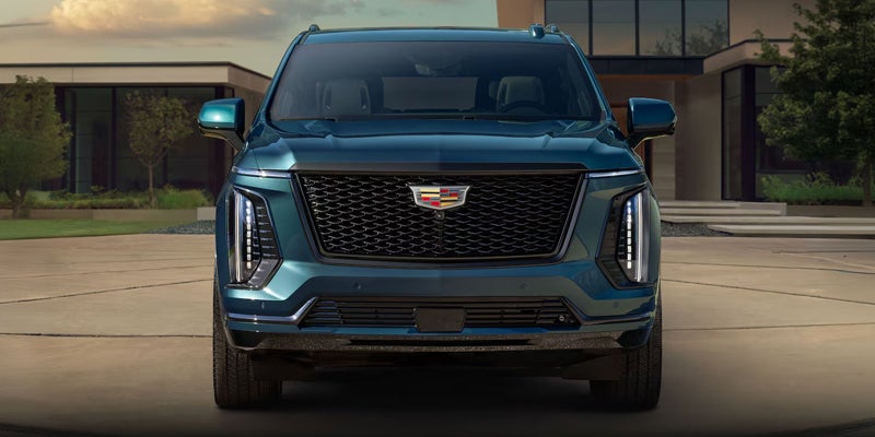 Front-facing view of a dark teal Cadillac Escalade parked in a driveway outside a modern home.