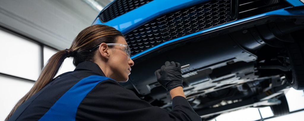Female automotive technician inspecting the underside of a vehicle in a service garage