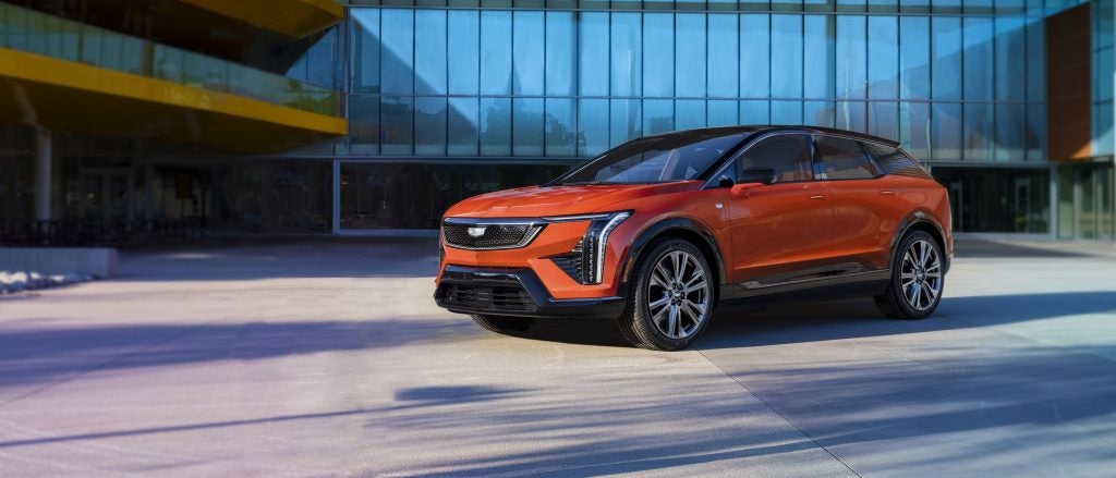 Orange Cadillac Optiq SUV parked in front of a modern glass building.