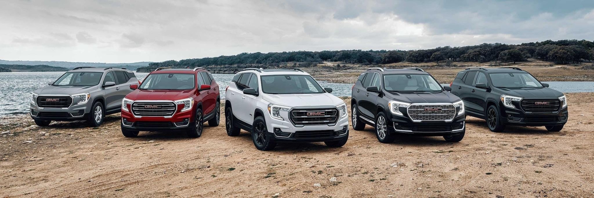 Five GMC SUVs in various colors parked in a row on a lakeshore