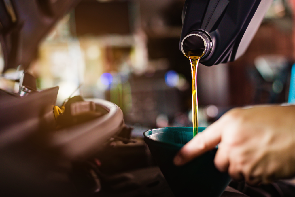Close-up of motor oil being poured from a black container into a car engine through a funnel. The image conveys a sense of maintenance and care.
