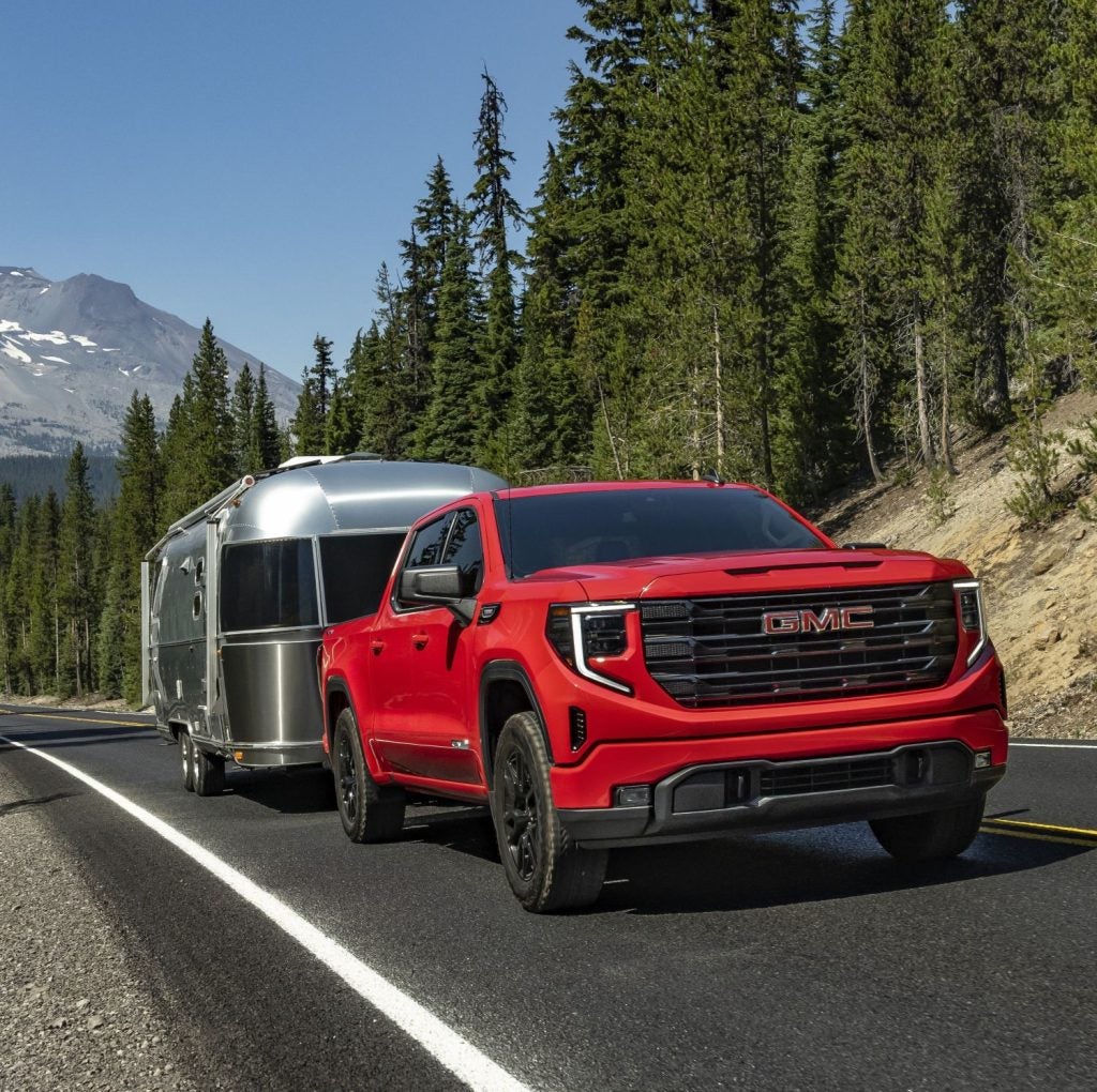 2026 GMC Sierra 1500 Elevation Crew Cab Short Box in Cardinal Hauling/Towing Airstream Trailer/Camper; 3/4 Passengers side Front; Road shot/motion; Forest and Mountains in background