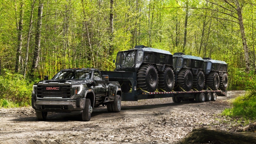 GMC Sierra HD driving a load of UTVs through a forest