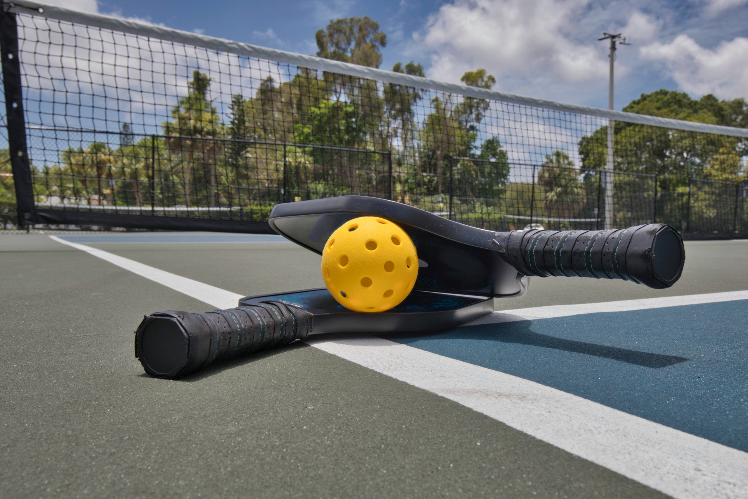 pickleball paddleson the ground in front of a pickleball court