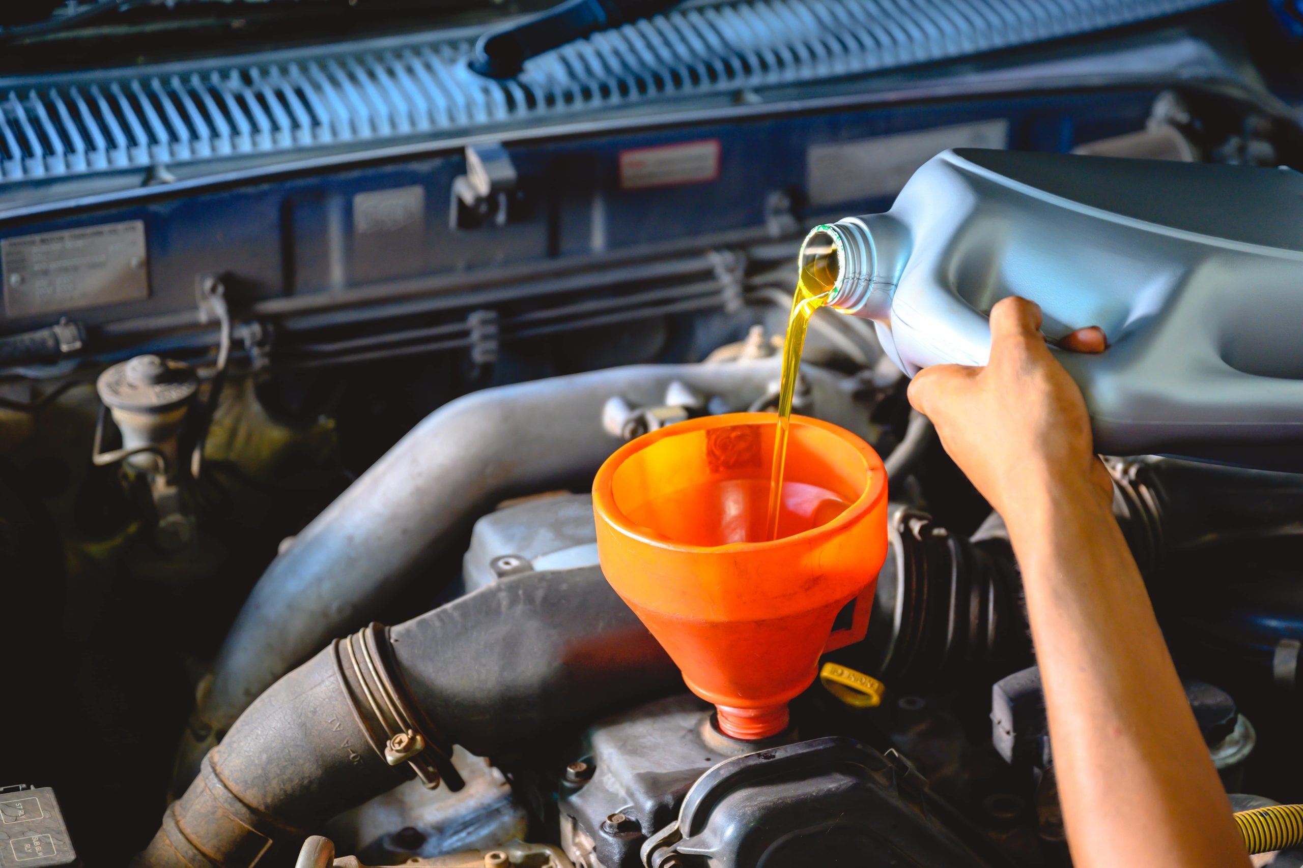 Mechanic pouring fluids into a car's engine with a funnel