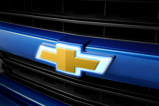 Close-up of a Chevrolet front grille with a prominent gold bowtie emblem centered on a sleek blue surface, conveying a sense of strength and style.