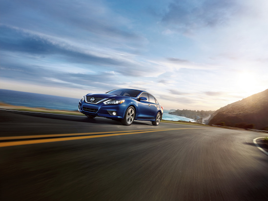 A blue car drives on a coastal road with the ocean on the left. The sky is partly cloudy, and the sun is low, casting a warm glow. Sense of freedom and adventure.