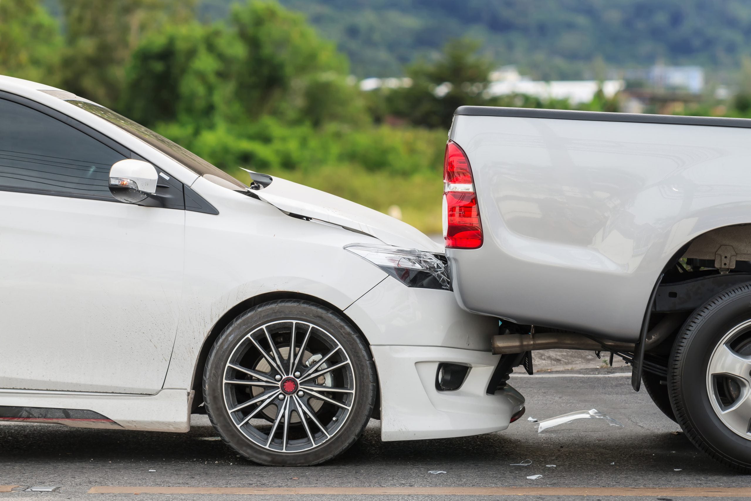 A white car rear-ended by a pickup truck, with visible damage to both vehicles.