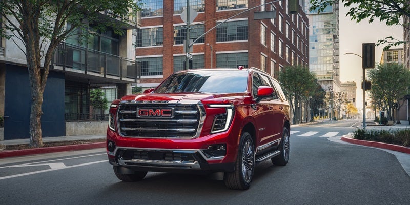 2026 GMC Yukon SUV driving through a downtown street in Wichita Falls, TX, showcasing a bold grille, modern design, and full-size luxury presence.