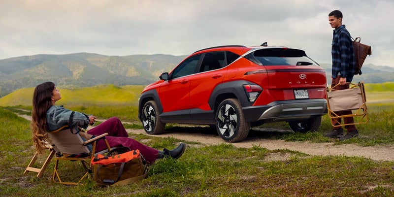 A red 2026 Hyundai Kona parked next to two individuals sitting on a bench in Wichita Falls, TX.
