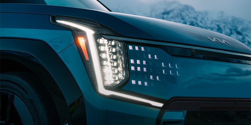 Close-up of a modern 2025 Kia EV9 SUV's front headlight with LED lights and sleek design.