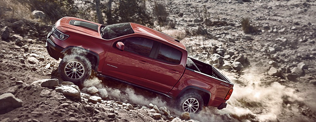 A red pickup truck powers uphill on a rocky, dusty terrain, exuding ruggedness and strength. Dust trails behind, emphasizing motion and adventure.